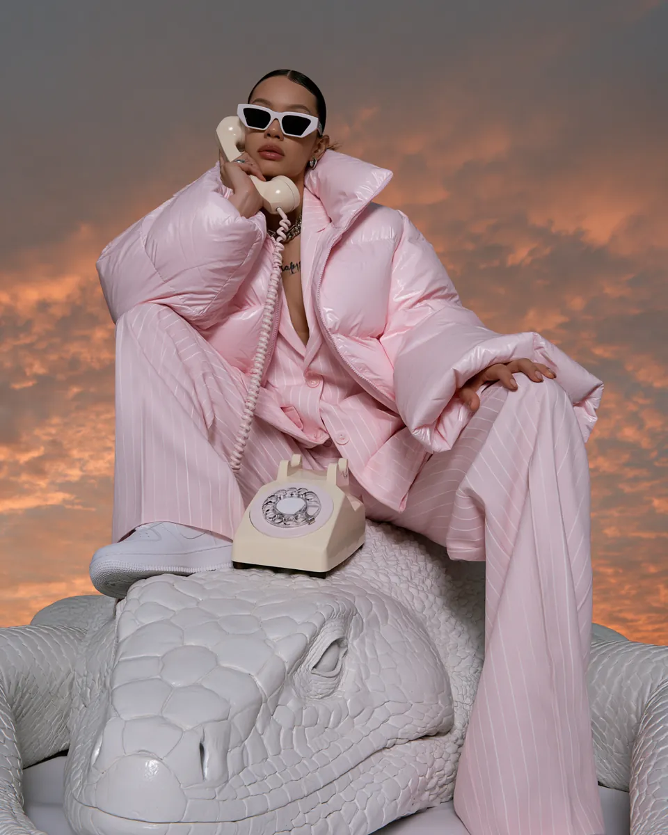 Model in pale pink tailoring holding a rotary telephone while seated on a giant white reptile.