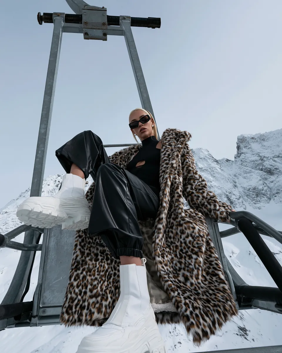 Low-angle winter fashion study with a leopard coat, black trousers and white platform boots.